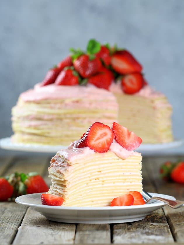 Piece of Strawberry Lemon Creme Crepe Cake on a plate with the rest of the cake in background 