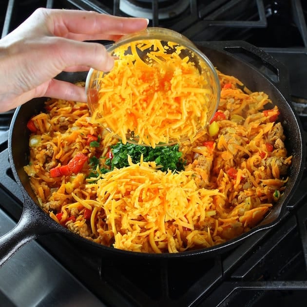 Adding shredded cheddar to a breakfast skillet