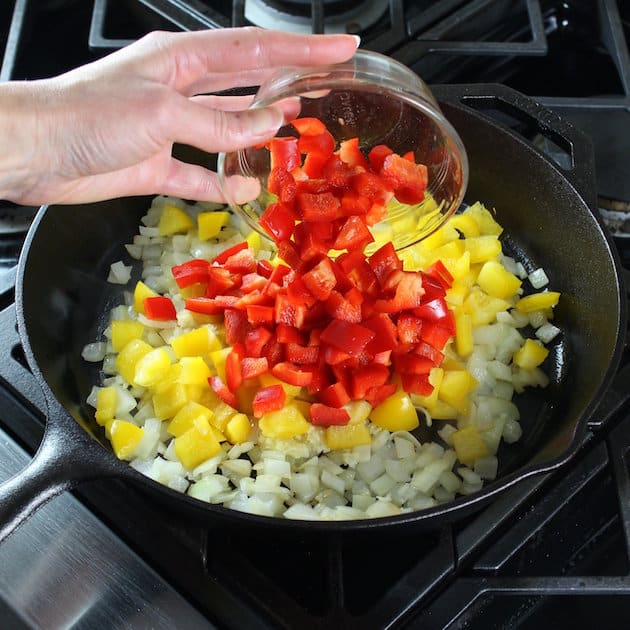 Adding chopped peppers into a skillet with onions and garlic