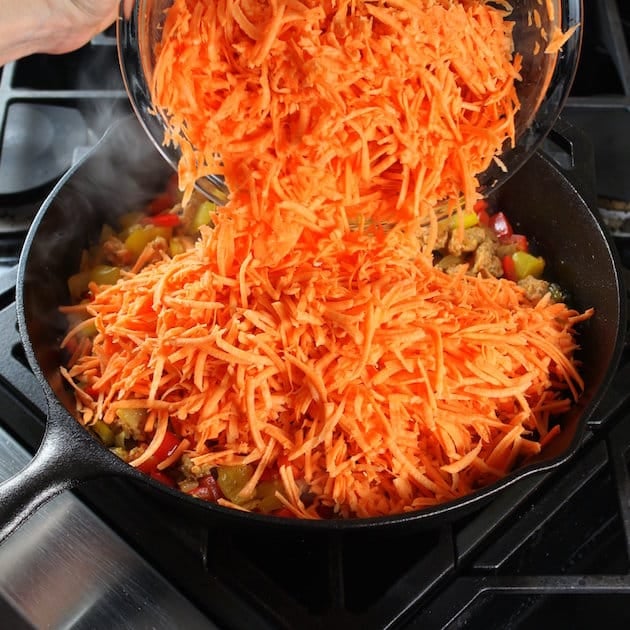 Adding shredded sweet potatoes to a breakfast skillet