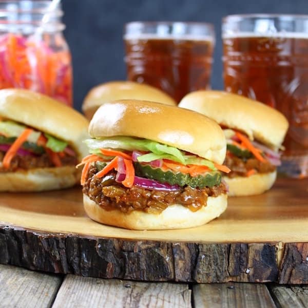 Four Asian sloppy joe sliders on a wooden platter with beers