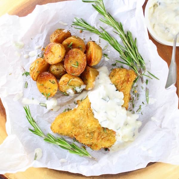 Breaded fish filet with tartar sauce and roasted baby potatoes on parchment paper