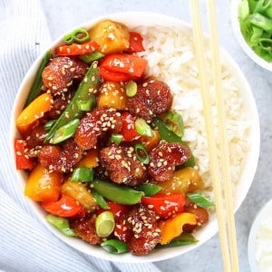 Sweet and sour shrimp with peppers, peas and rice in a bowl with chopsticks
