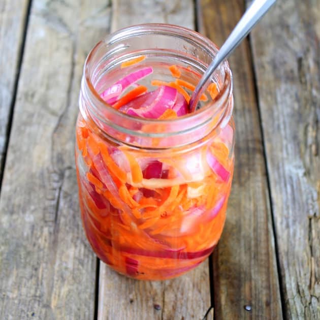 A close up of a mason jar with pickled carrots and onions