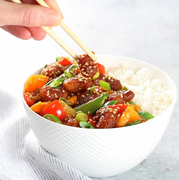 Hand holding chopsticks in a Sweet and Sour Shrimp Rice Bowl 