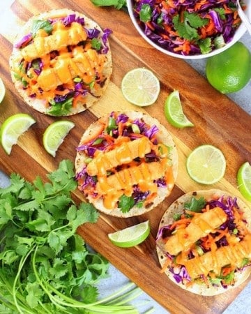 Three fish tacos on a cutting board with slaw and bang bang sauce