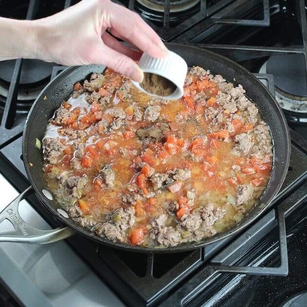 Adding all spice to tomato and lamb meat mixture on stovetop
