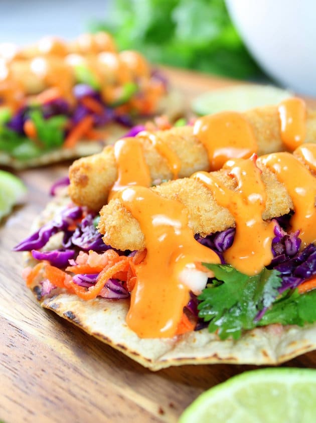 Eye level close up fish taco on cutting board with orange creamy sauce 