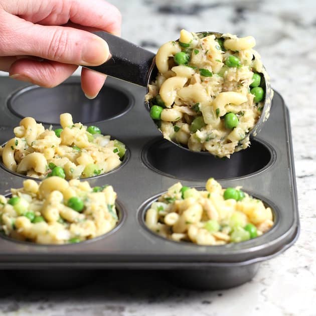 A person adding tuna casserole to muffin tin