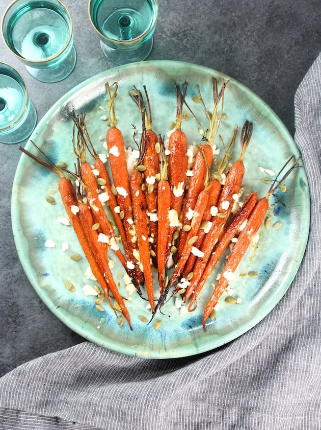 Whole carrots on a platter with goat cheese and pepitas