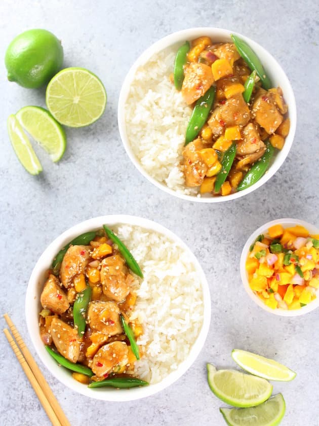 Two bowls of asian chicken stir fry with a side dish of mango relish