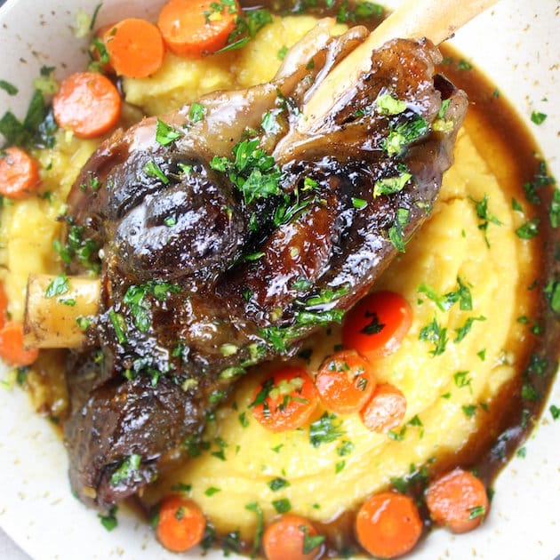 Close up slow cooked glazed lamb shank in a bowl of parmesan polenta 