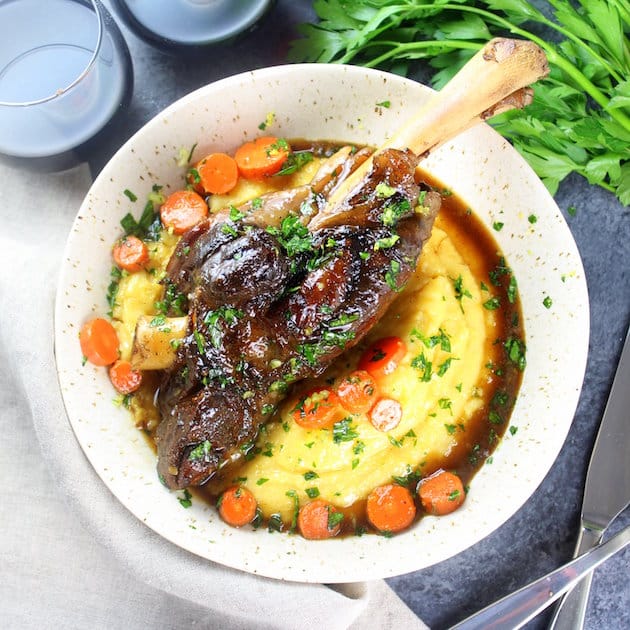 SLow cooked glazed lamb shank in a bowl of parmesan polenta with cooked carrots and red wine