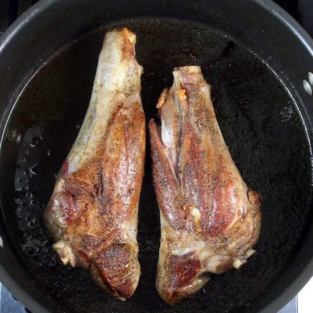 Two lamb shanks searing in a Dutch oven