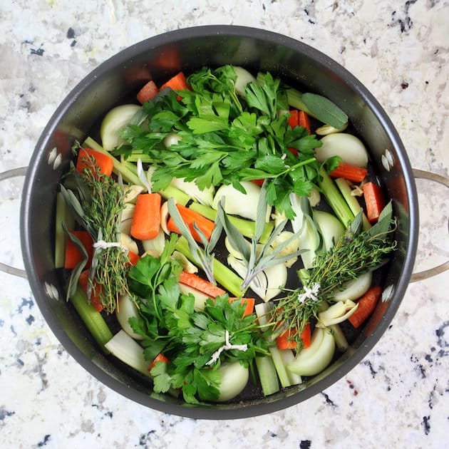 Carrots, celery, onion, and herb bundles in a dutch oven ready for cooking