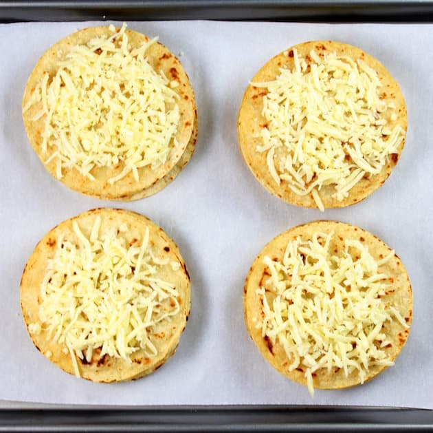 Shredded white cheese on top of four tortillas on a baking sheet