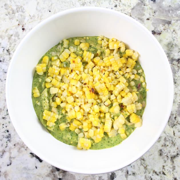 Adding corn to mixing bowl with green poblano sauce