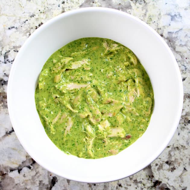 Shredded chicken mixed into green poblano sauce in a white mixing bowl