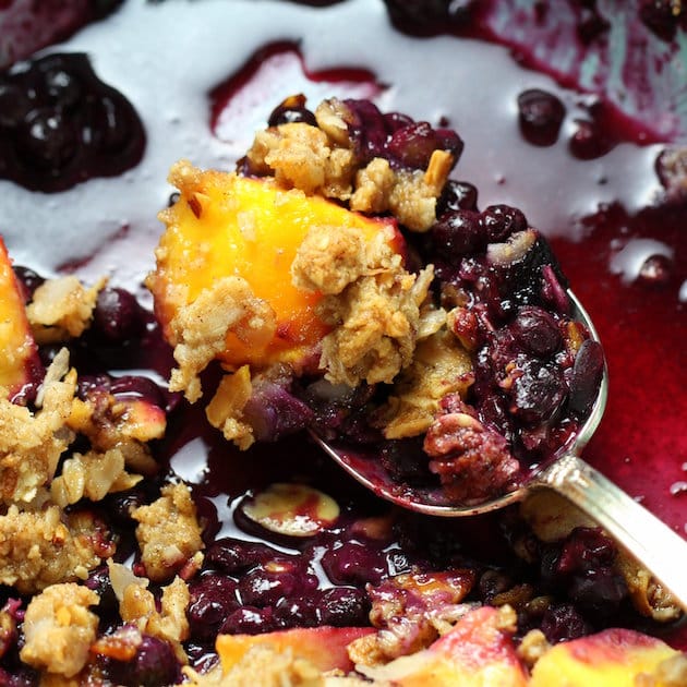 Close up spoon scooping a bite of mango blueberry coconut crumble