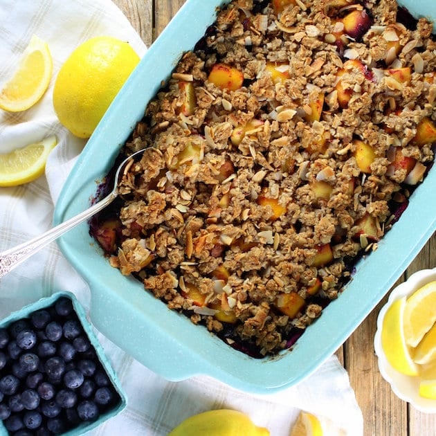 Tropical Blueberry Mango Coconut Crumble in a casserole dish next to fresh lemons and blueberries 