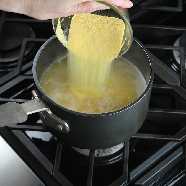 Adding dry polenta to pot on stovetop