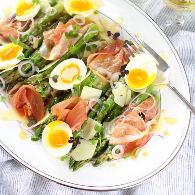 An asparagus salad on a platter with prosciutto and lemon- Dijon dressing.