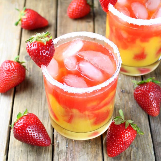 Red and yellow swirled drink in a cocktail glass with salted rim and strawberry garnish