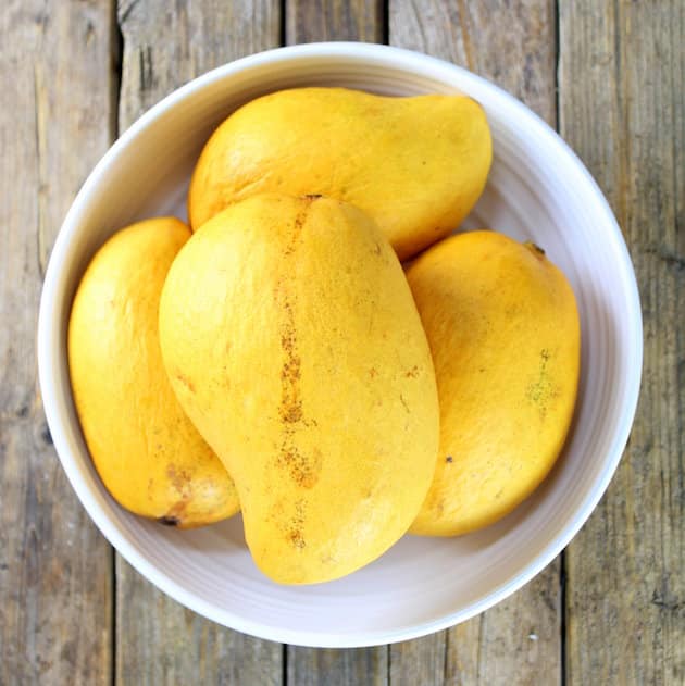 four yellow honey mangoes in a bowl