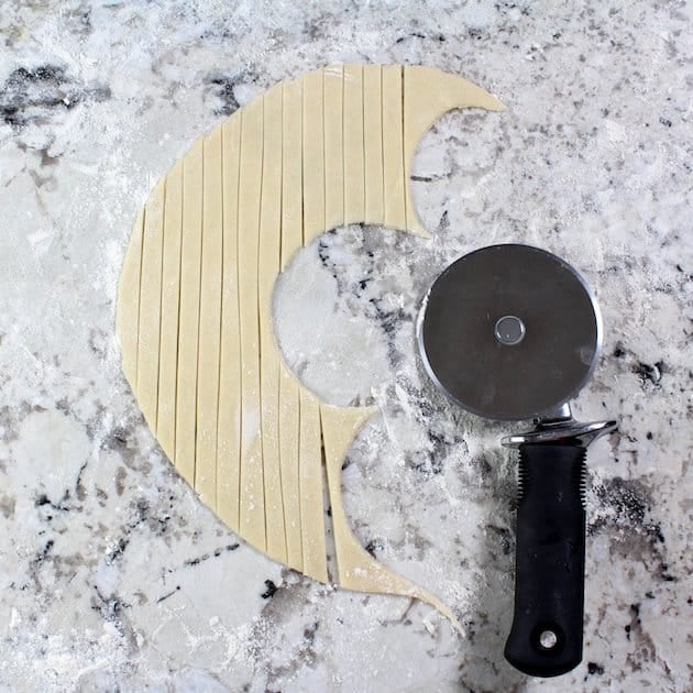 Using pizza cutter to cut pastry dough into thin strips