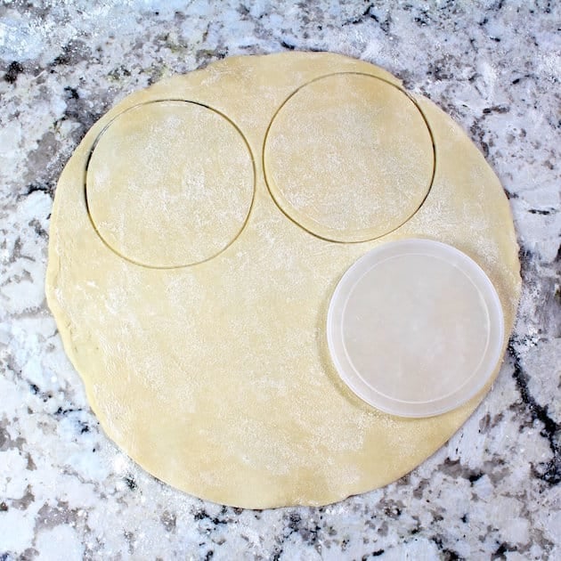 Cutting pastry dough into circles on granite countertop