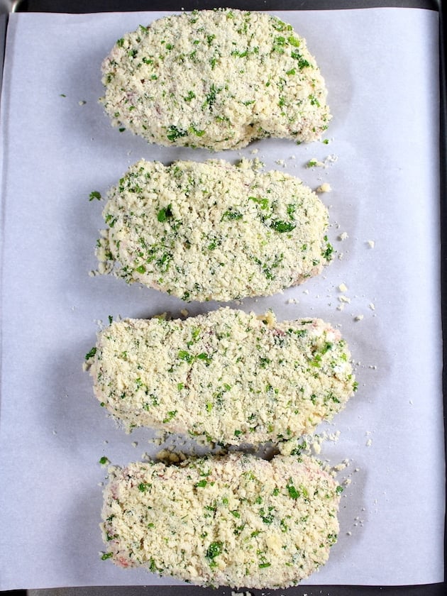 Four breaded pork chops on a baking sheet ready to cook