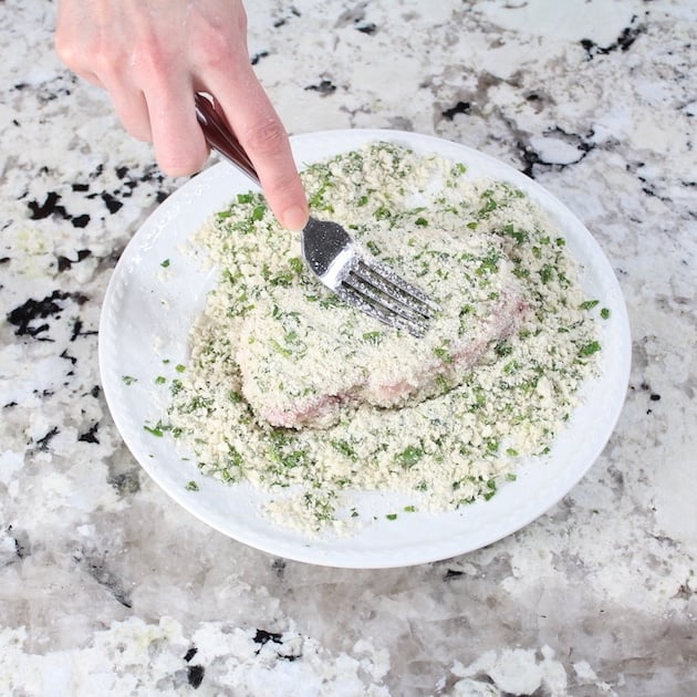 Using a fork to coat pork chop in bread crumbs