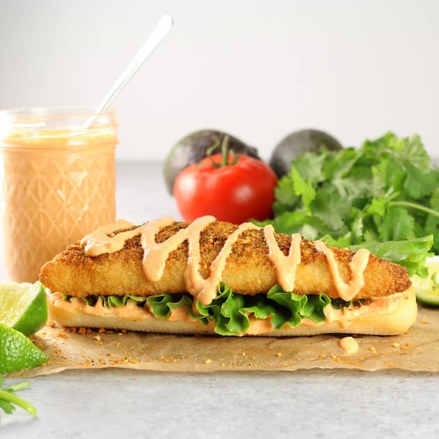 An open faced fish sandwich with mason jar of baja sauce behind