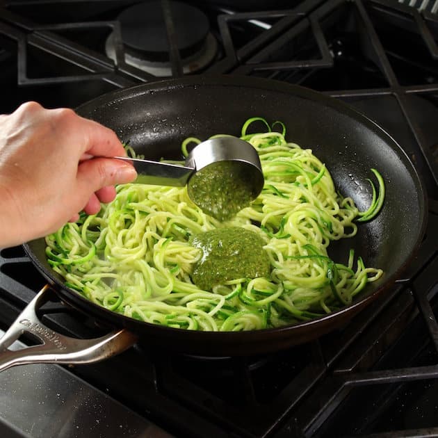 Adding pesto sauce to zucchini noodles in a skillet