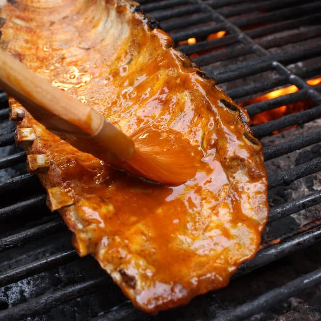 Brushing BBQ sauce onto rack of ribs cooking on grill