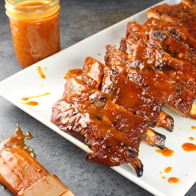 A platter of ribs with BBQ sauce on them and a mason jar of BBQ sauce and basting brush on the side.