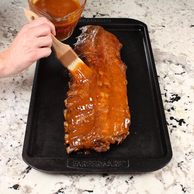 Basting a rack of ribs on cookie sheet before grilling