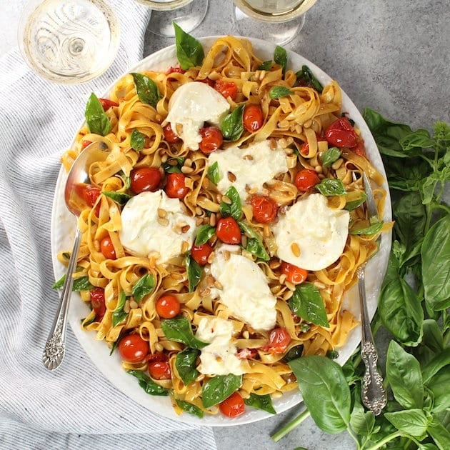 Plate of Tagliatelle with Burrata, Tomatoes, and Pine Nuts with wine glasses