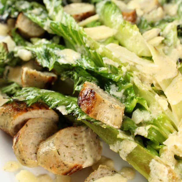 A close up of a plate of caesar salad with sliced chicken sausage