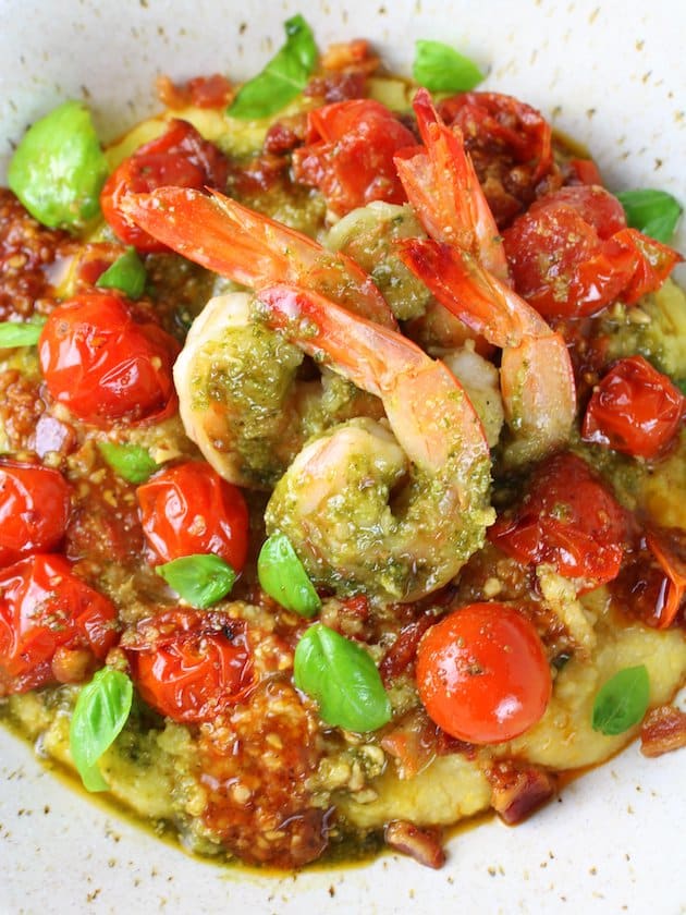 Closeup of shrimp in pesto sauce on tomato polenta bed