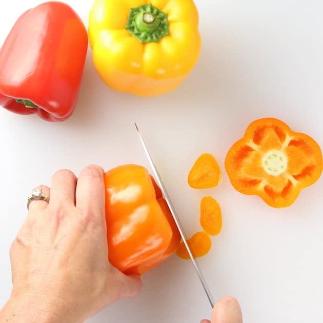 Cutting the bottom off an orange bell pepper so it doesn't tip over while cooking.