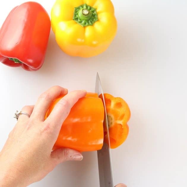 Slicing orange bell pepper on a cutting board.