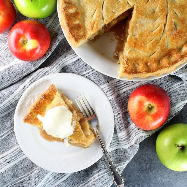 Piece of homemade Apple Pie topped with vanilla ice cream on plate.