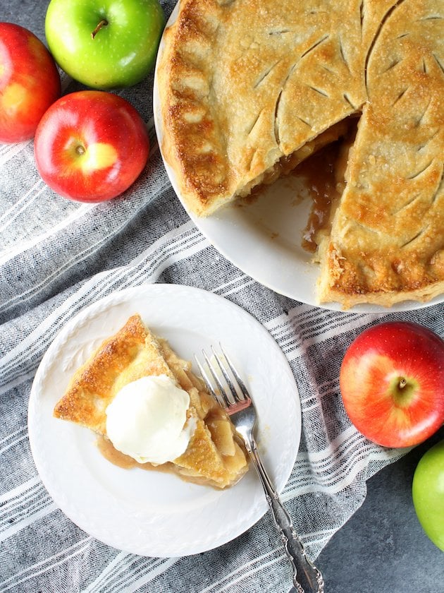 Apple Pie topped with vanilla ice cream on a table with napkins and apples.