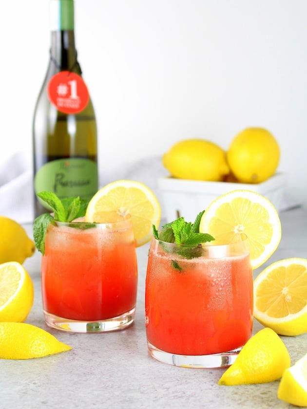 Two glasses of red prosecco spritzer with wine bottle in background