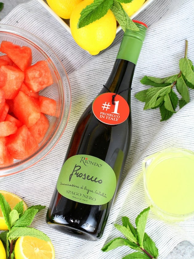 A bowl of fruit sitting on a table, with Prosecco and Watermelon