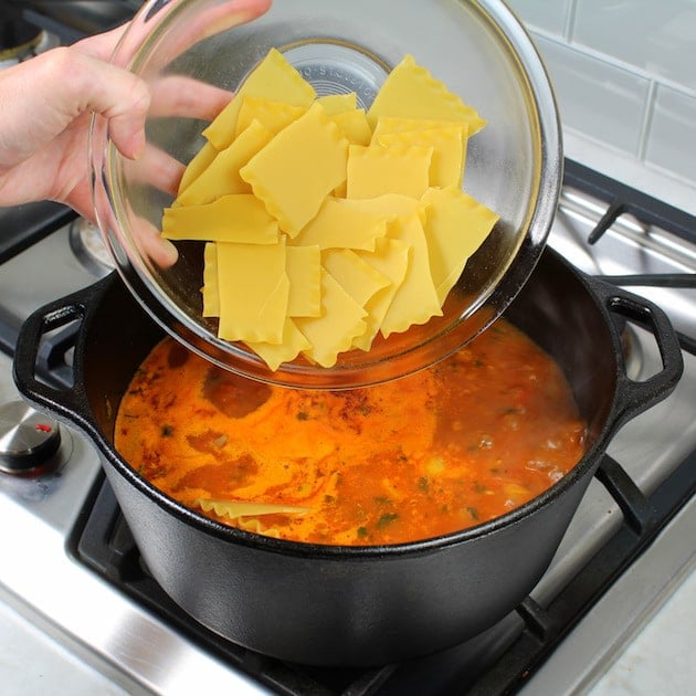 Adding lasagna pasta to soup pot with red sauce