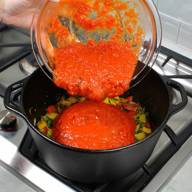 Adding red sauce to large soup pot with vegetables