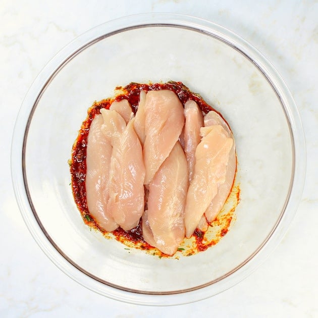 Raw chicken breasts on harissa marinade in a glass bowl