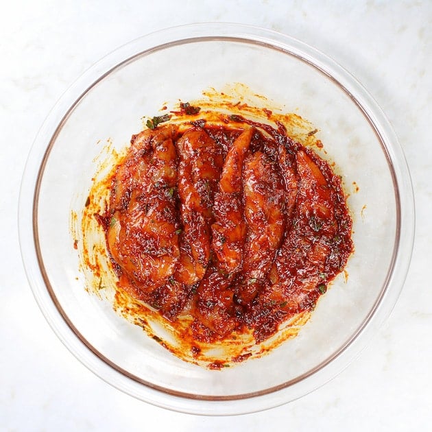 bowl of chicken tossed in harissa marinade in a glass bowl